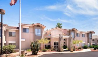 The hotel’s exterior has a fluttering USA flag flying from a flagpole and greenery including bushes, small trees, and a cactus.