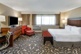 Double bed guest room in Sonesta Los Angeles Airport LAX, featuring armchair, TV, and workspace desk and chair.