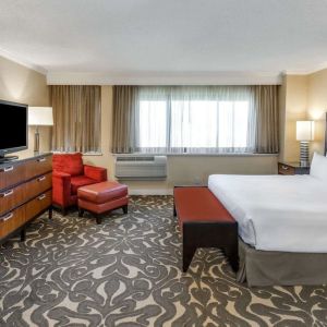 Double bed guest room in Sonesta Los Angeles Airport LAX, featuring armchair, TV, and workspace desk and chair.