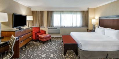 Double bed guest room in Sonesta Los Angeles Airport LAX, featuring armchair, TV, and workspace desk and chair.