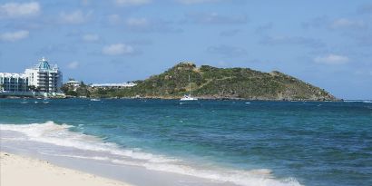 Waves coming on shore with view of resort buildings and mountainous island in distance. 