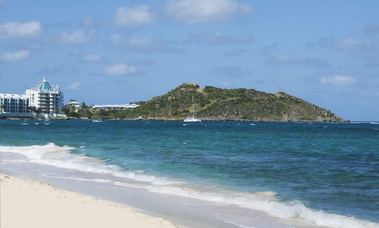 Waves coming on shore with view of resort buildings and mountainous island in distance. 