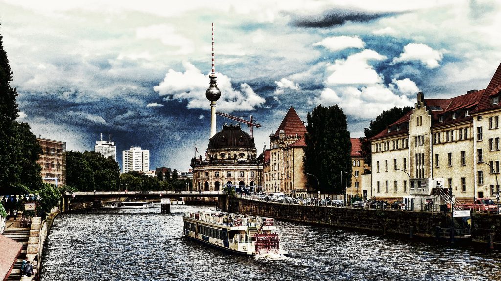 A boat navigating the canal in Berlin with the Berliner Fernsehturm in the backdrop.