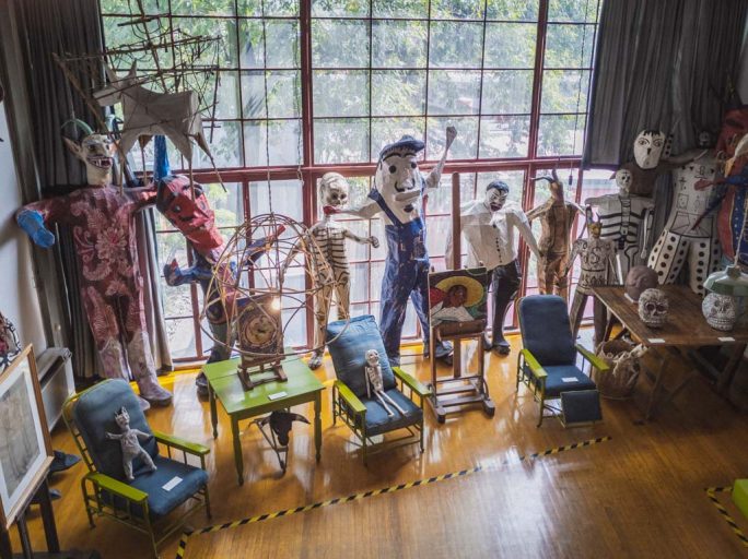 A variety of multi colored life size puppets lean against a floor to ceiling glass window grid.