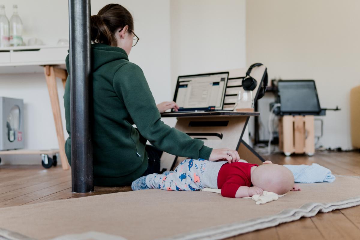 Mom rubs baby's back as she works from home on laptop.