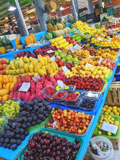 An overflowing market display of fresh tropical fruits including cherries, figs, mangoes, dragonfruit, grapes, and berries.