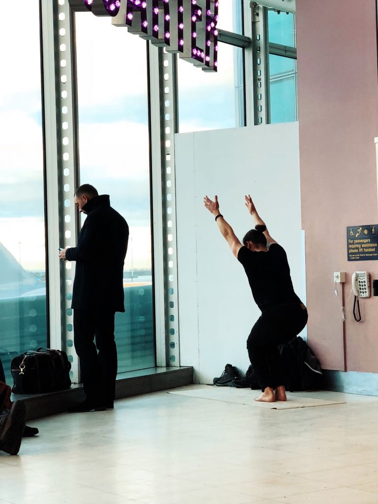 Man stretches arms high in yoga pose in a corner of the airport before a long flight.