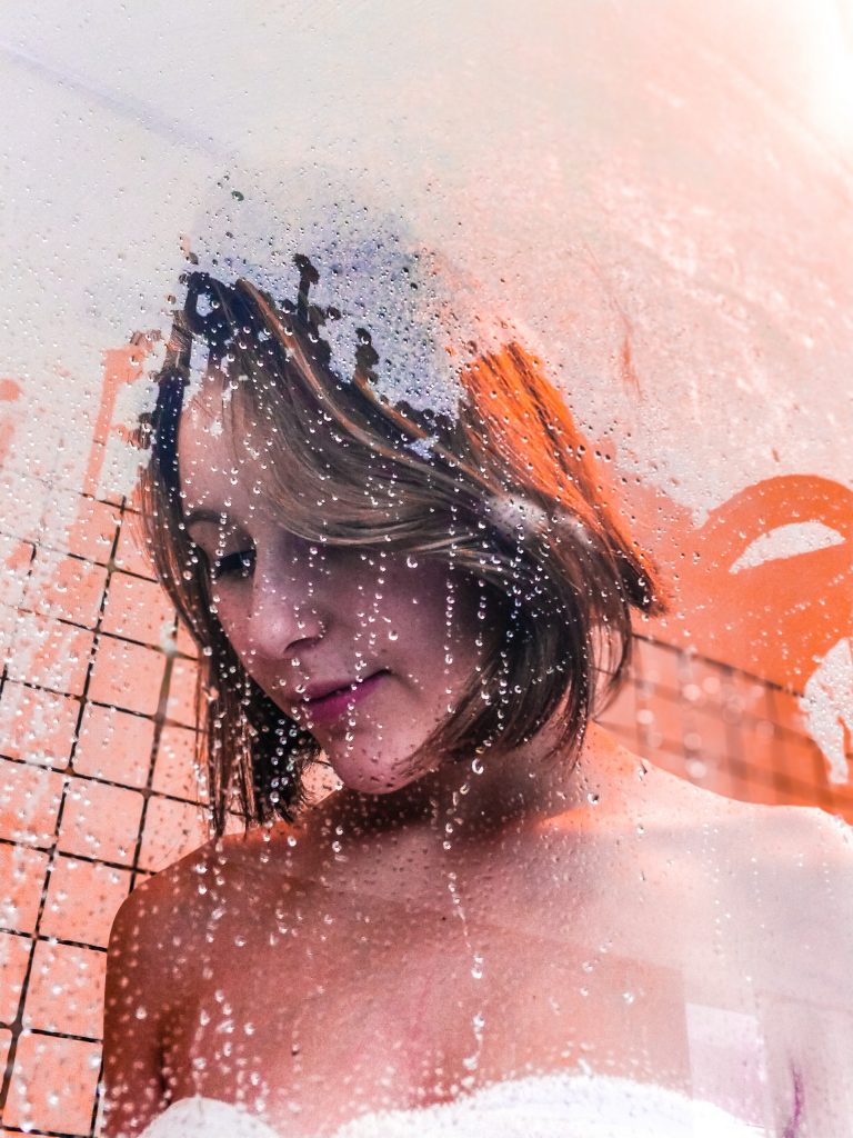 Woman peacefully staring down while showering with suds streaking on glass.